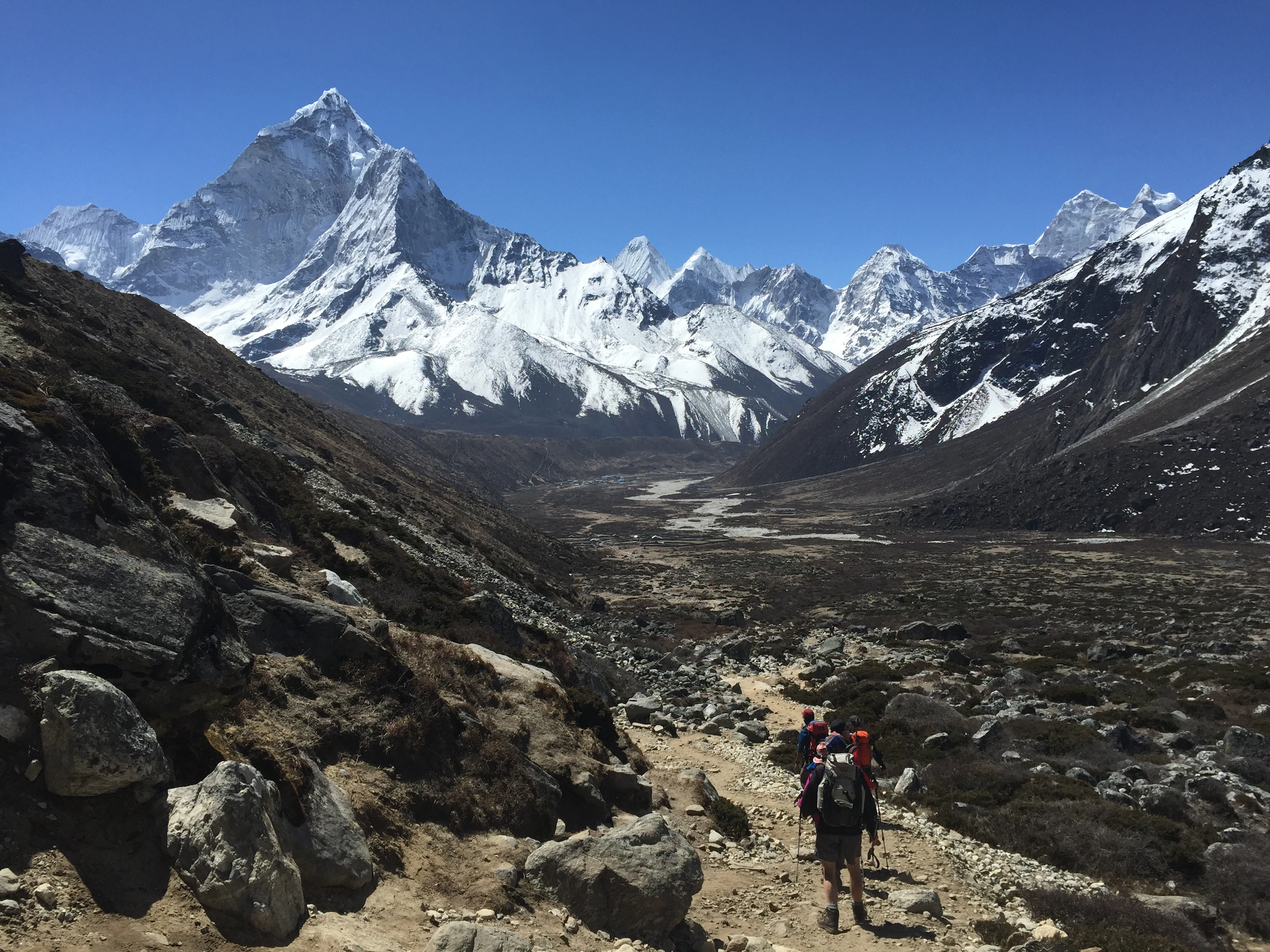 Žygeiviai akmenuotu taku aukštikalnių slėnyje po snieguotomis Himalajų viršūnėmis, Nepalas