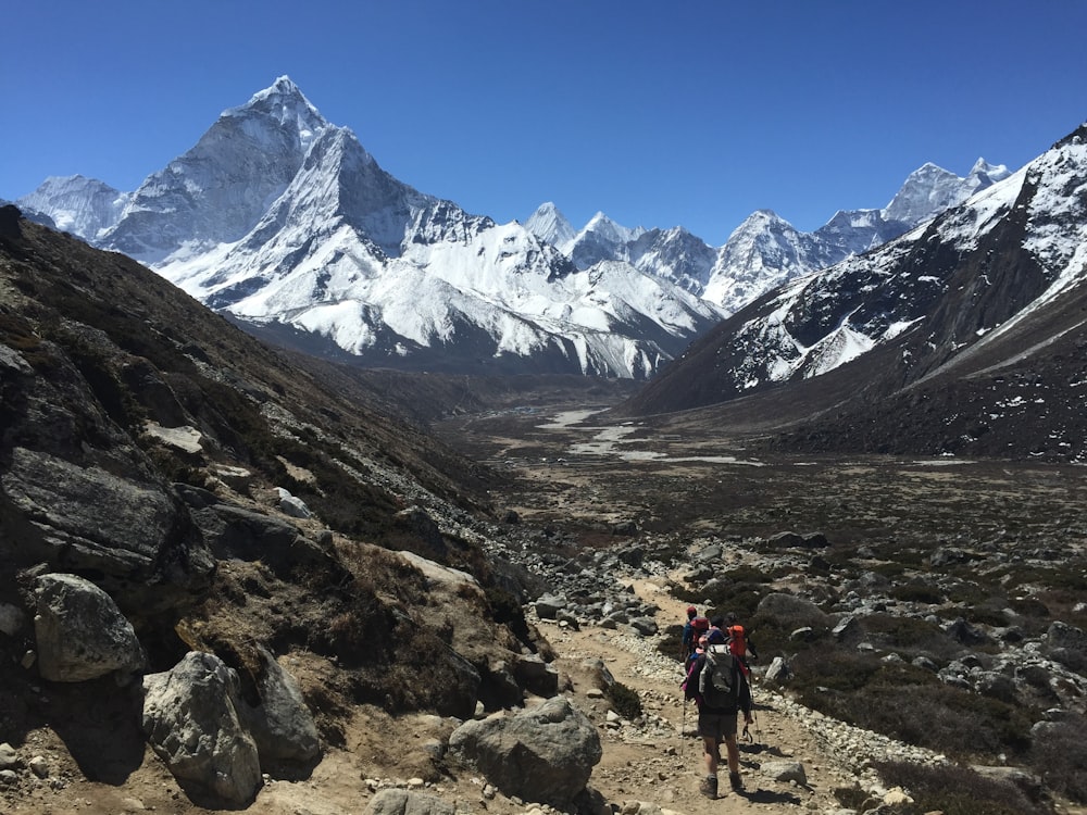 person in red jacket and black pants walking on rocky mountain during daytime