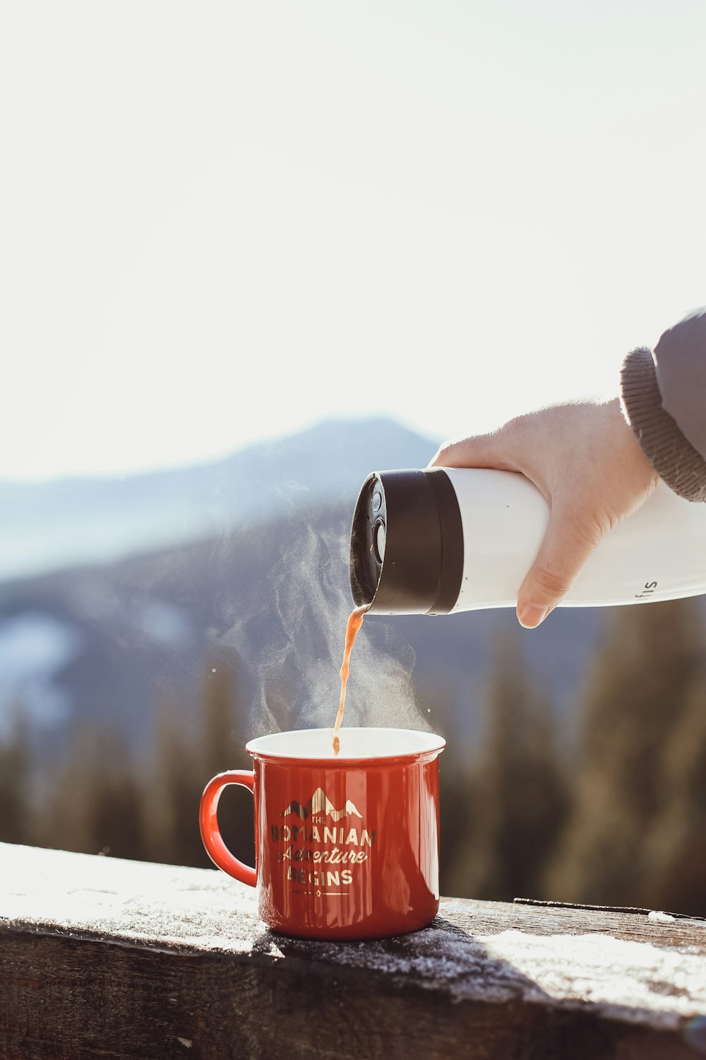 person pouring water on red ceramic mug