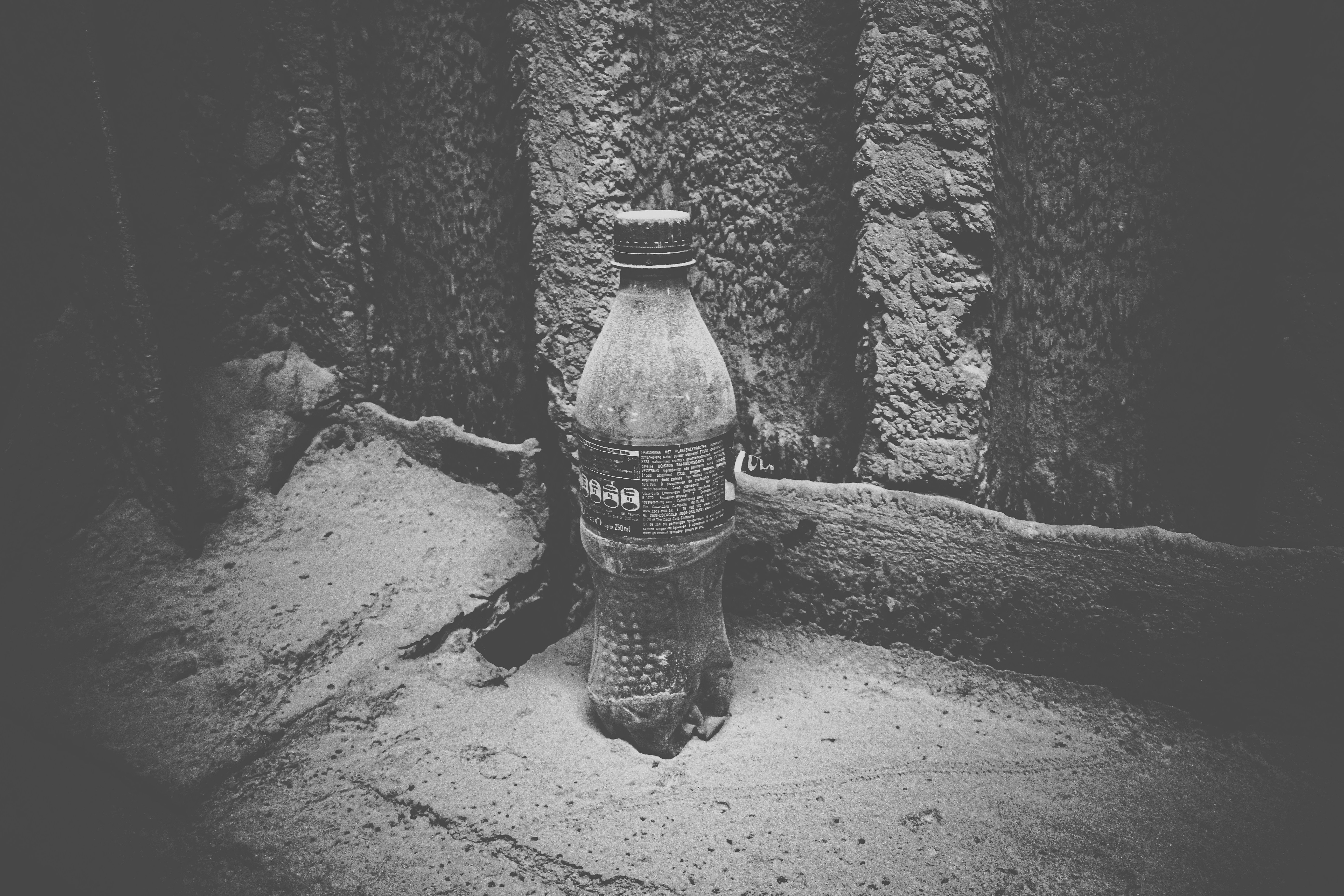 foto em tons de cinza da garrafa de plástico na areia