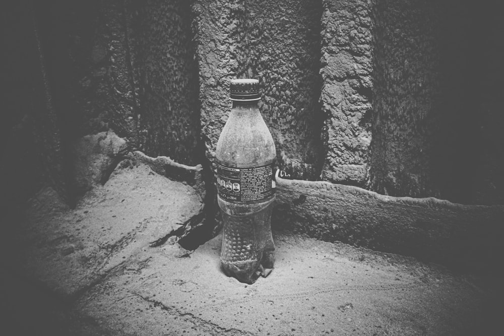 grayscale photo of plastic bottle on sand