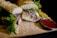 A sandwich stuffed with various fresh ingredients such as lettuce and purple cabbage, placed on a wooden board. Next to the sandwich are crispy golden fries and a small bowl of red ketchup, likely for dipping. The surrounding crumbs and casual placement suggest a casual dining setting.
