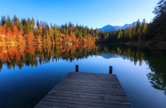 A serene lakeside view with a wooden dock stretching into calm waters framed by autumn leaves.