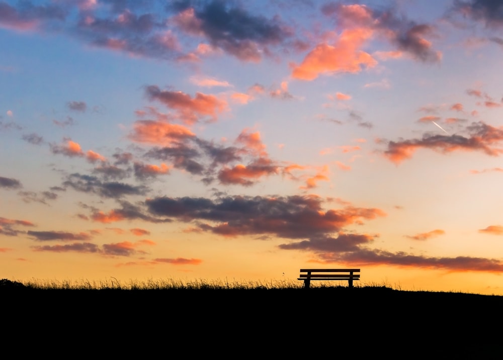 silhouette of bench on grass field during sunset