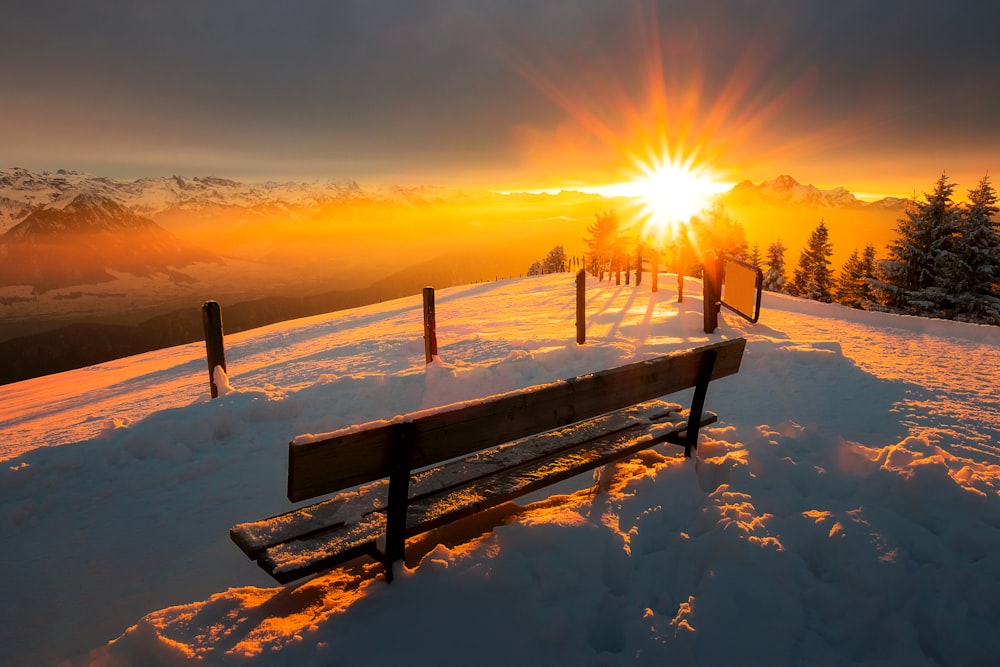 banco de madeira marrom no chão coberto de neve durante o pôr do sol