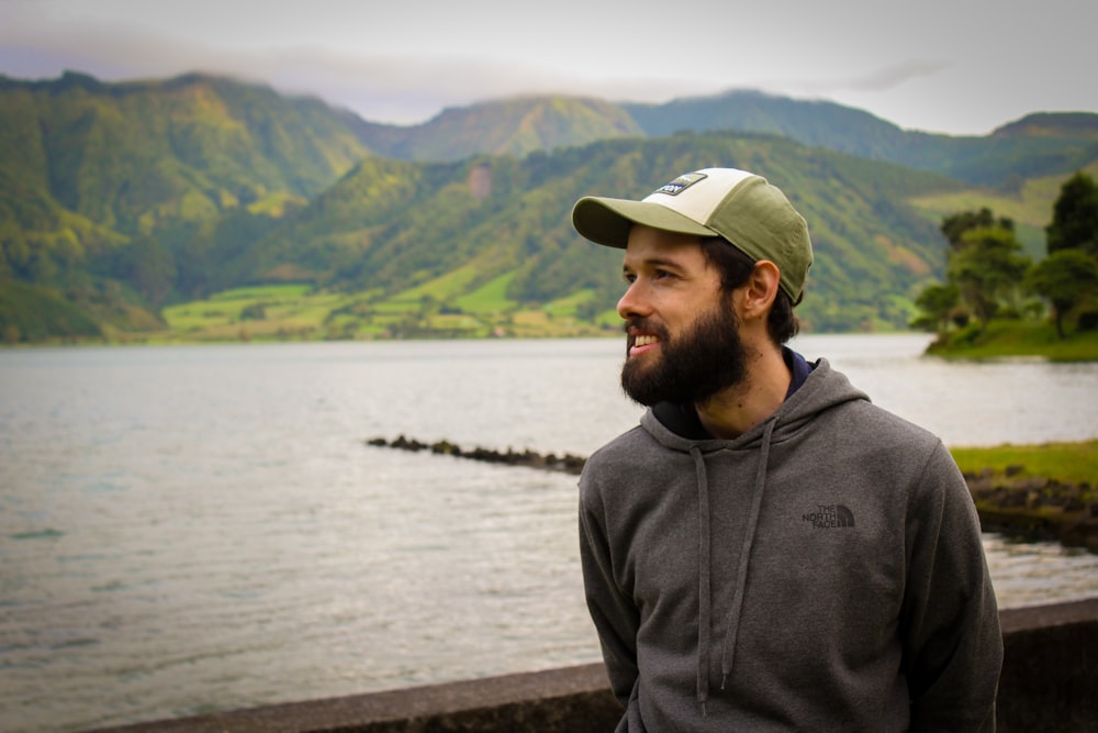 man in gray hoodie wearing white cap standing near body of water during daytime