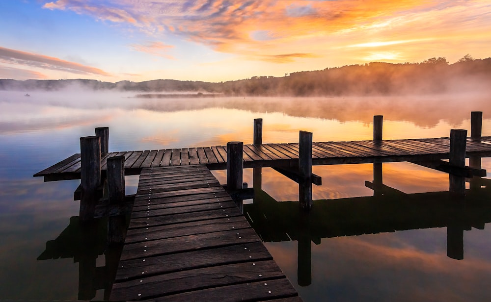 brown wooden dock on body of water during sunset