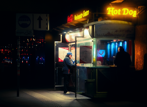 Happy customer enjoying a hot dog at a cozy street food stand in the evening.