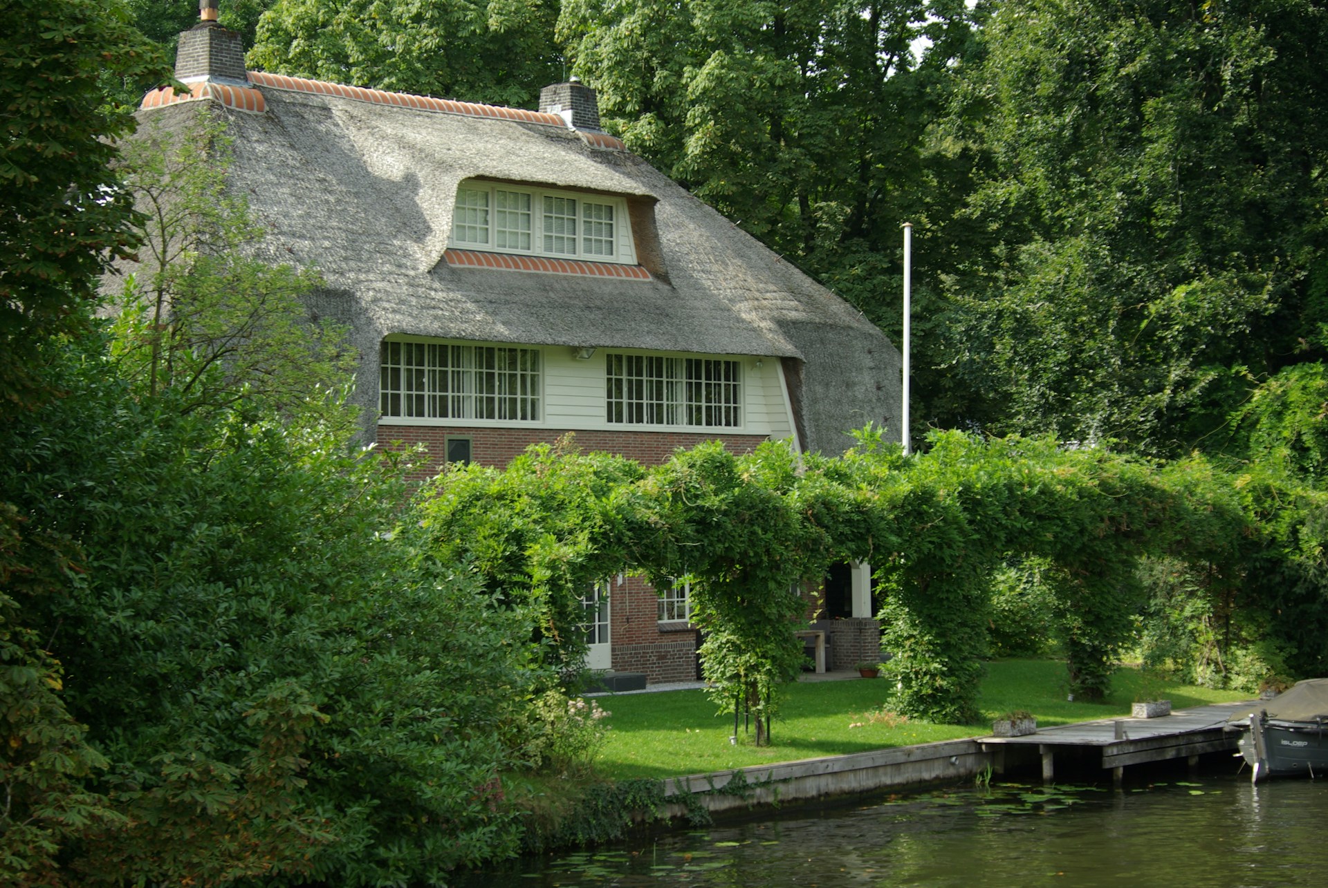 A cozy luxury cottage nestled among greenery, with a wooden deck overlooking the water.