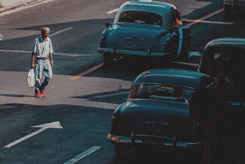 man in white jacket and black pants standing beside black porsche 911 on road during daytime