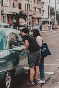 man and woman standing beside green car during daytime