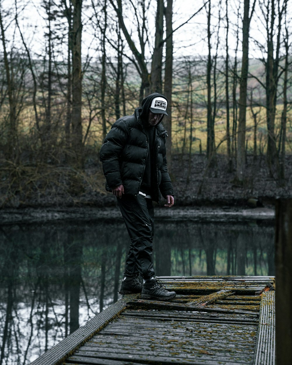 man in black jacket and black pants standing on brown wooden dock during daytime