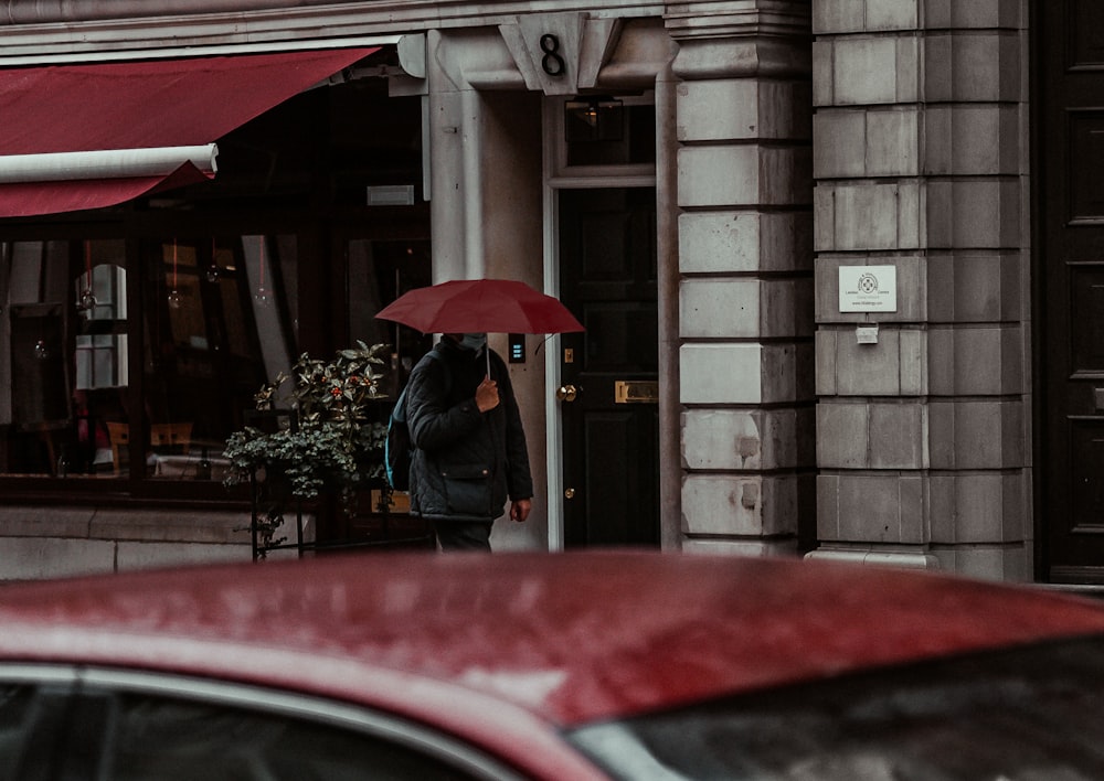Person in schwarzer Jacke mit rotem Regenschirm
