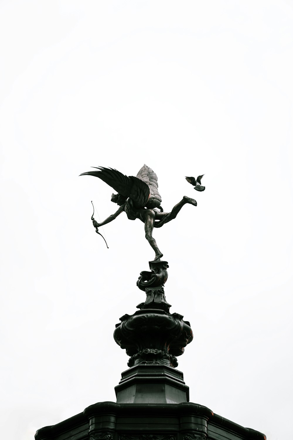 昼間の白い空の下に黒い鳥の像
