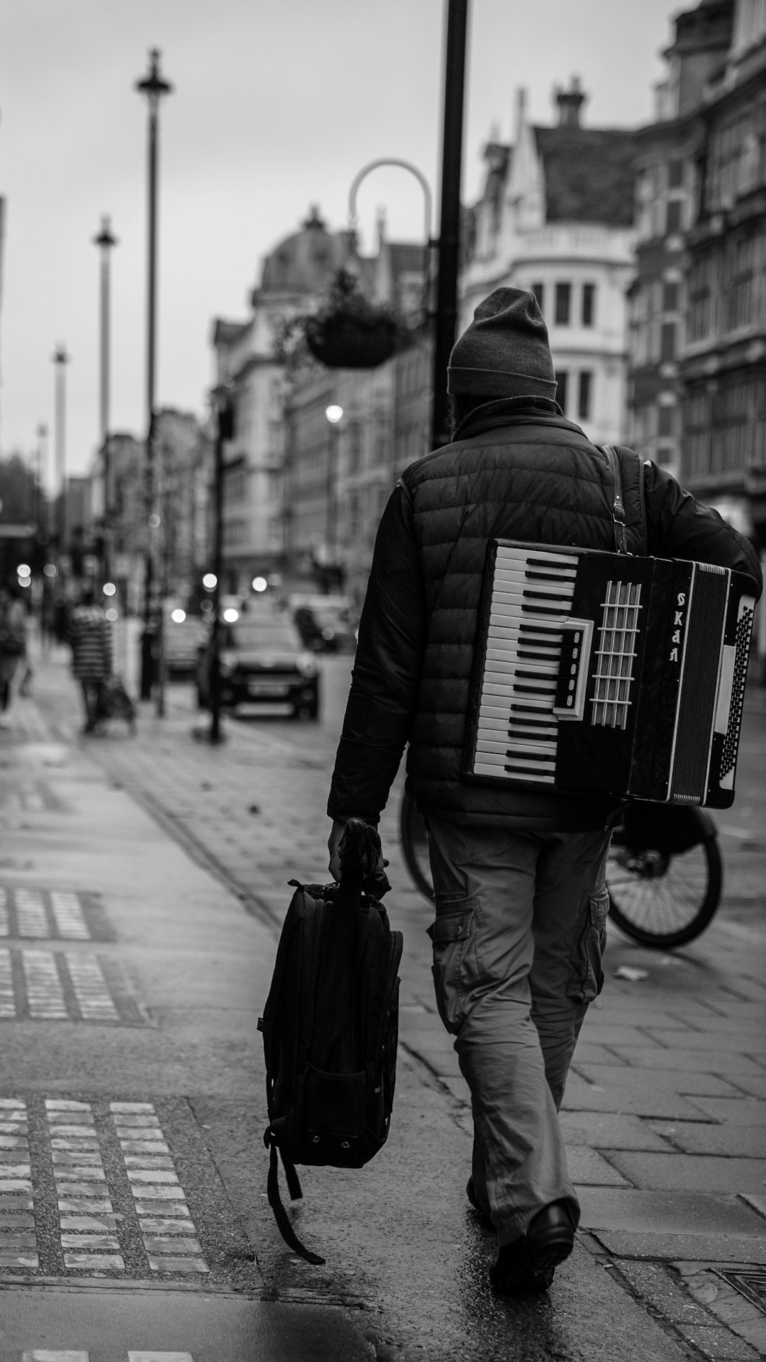 man in black jacket and pants playing piano on street in grayscale photography