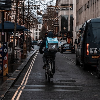 Delivery person on a bicycle navigating through city streets during the day.