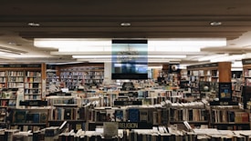 A large bookstore with numerous bookshelves organized by categories such as humanities, religion, new age, and law. The shelves are densely packed with a wide variety of books. Overhead lights illuminate the space, creating a cozy and inviting atmosphere.
