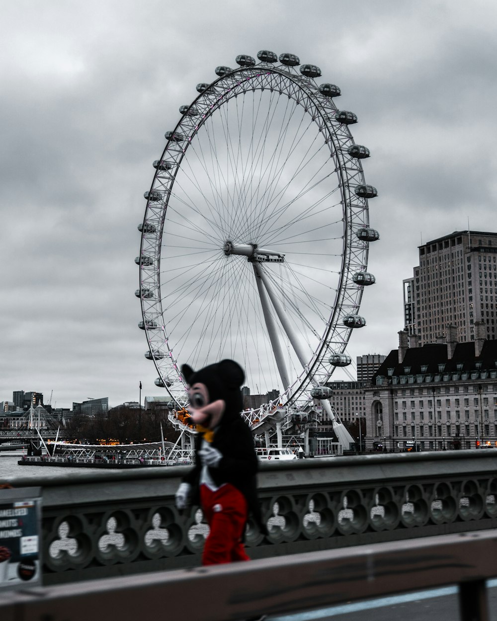 woman in black jacket and red pants standing on gray concrete bridge near ferris wheel during