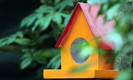 A vibrant handmade birdhouse painted in bright orange and green hues.