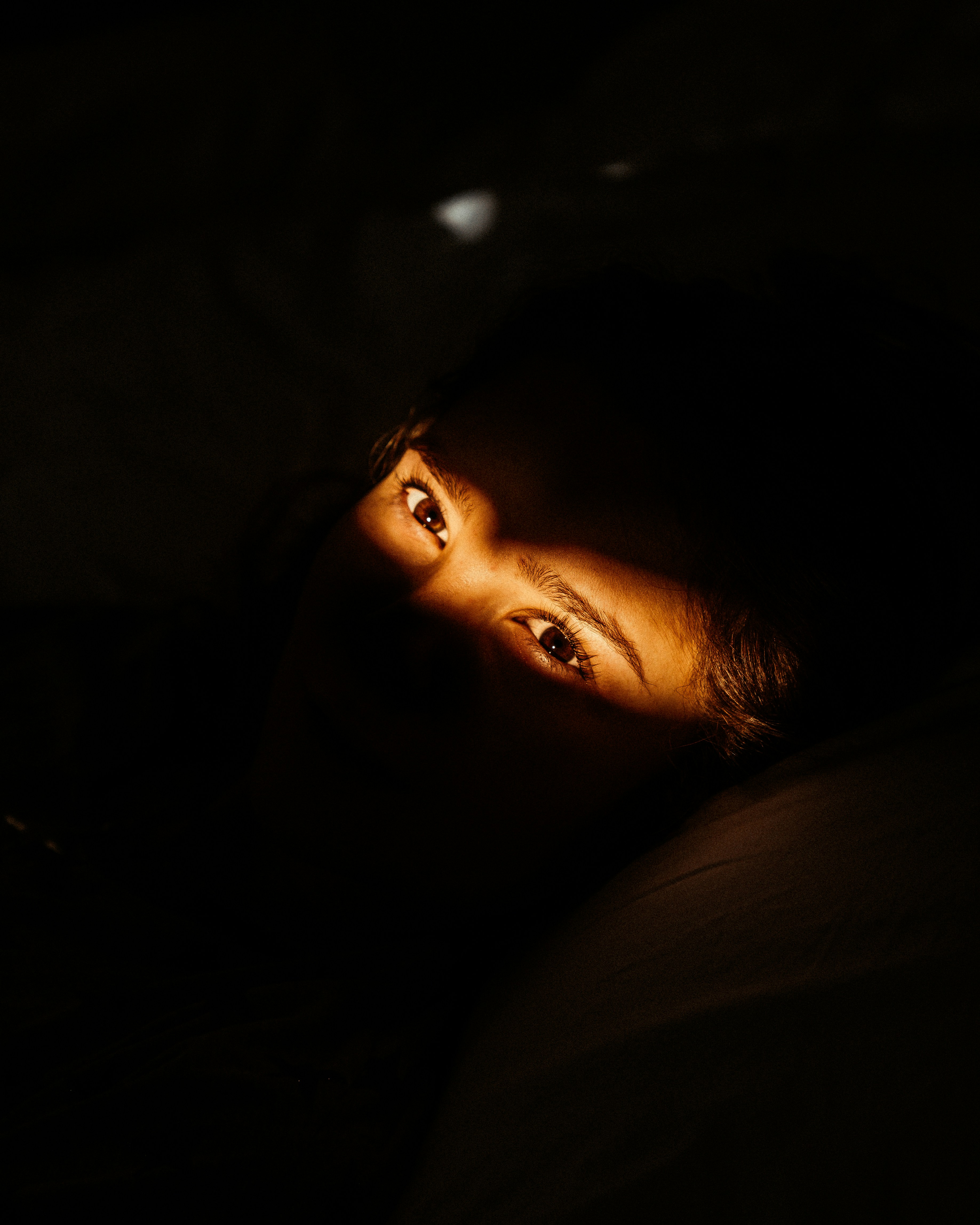 Portrait d'une femme allongée sur un lit. La photo est sombre et seul un bandeau de lumière éclaire ses yeux.