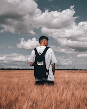 man in white and black adidas shirt standing on brown grass field under cloudy sky during