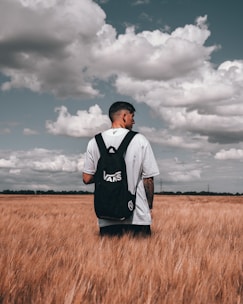 man in white and black adidas shirt standing on brown grass field under cloudy sky during
