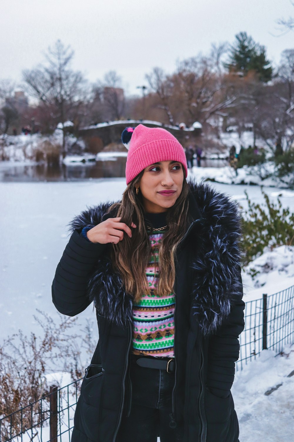 Mujer con chaqueta negra y gorra de punto roja de pie en un suelo cubierto de nieve durante el día