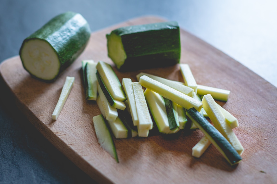 Sliced green zucchini on a wooden chopping board being prepped for grating