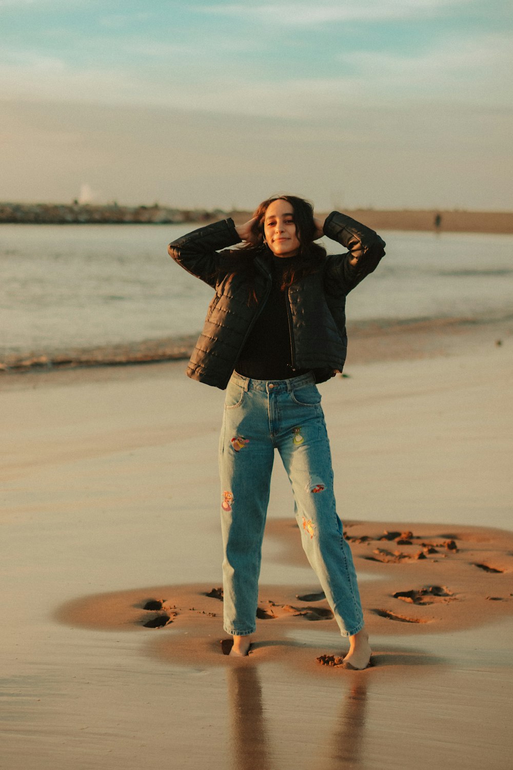 man in black leather jacket and blue denim jeans standing on brown sand during daytime