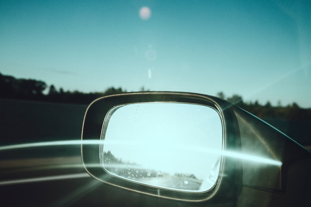 car side mirror showing green trees under blue sky during daytime