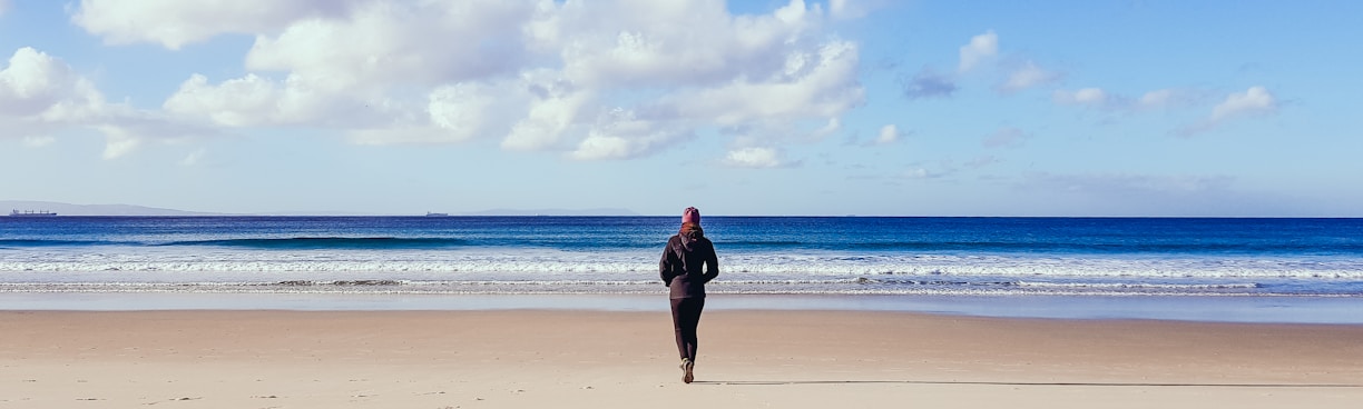 woman in black dress walking on beach during daytime
