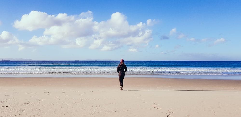 Frau in schwarzem Kleid, die tagsüber am Strand spazieren geht