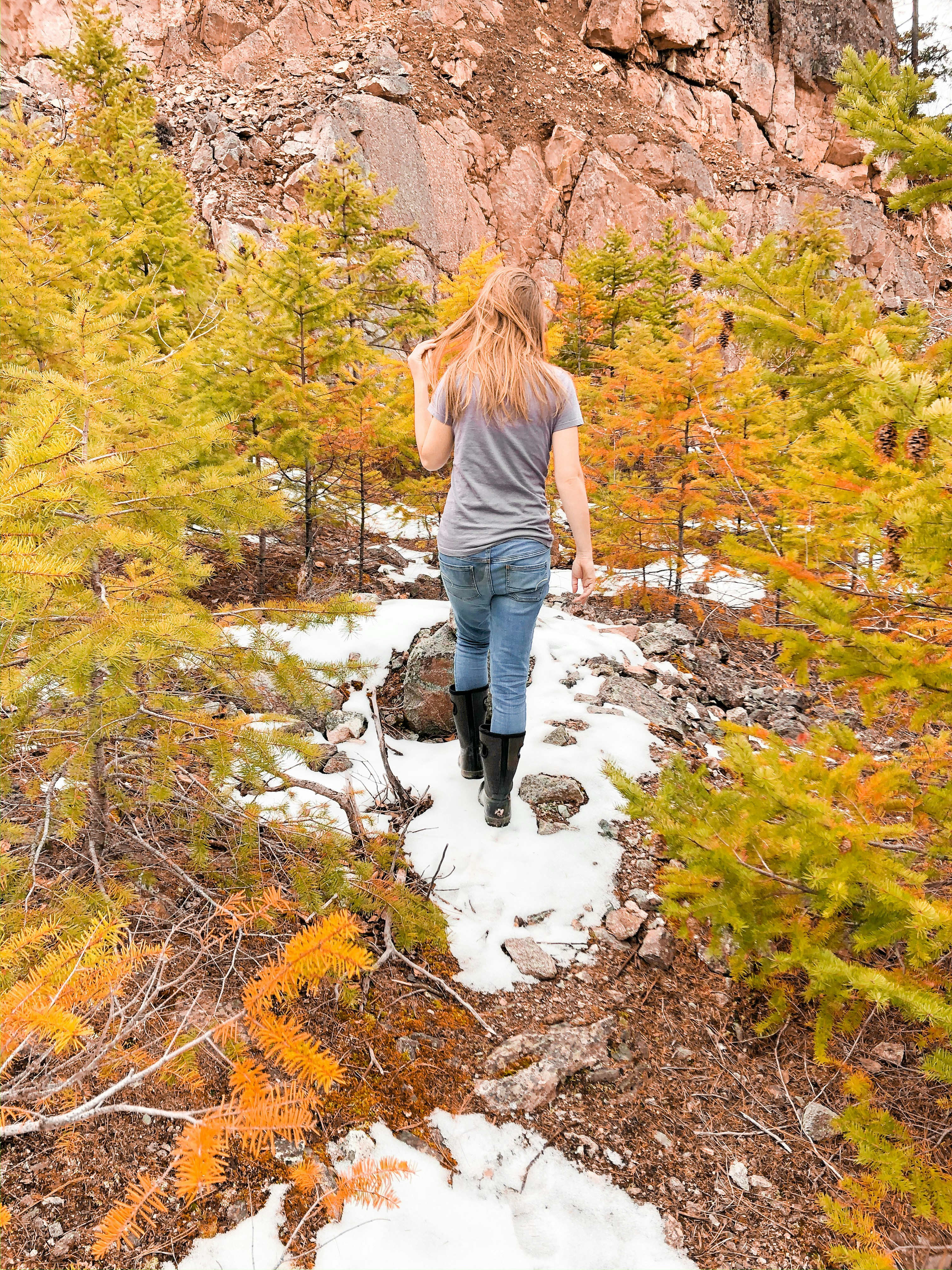 woman in gray long sleeve shirt and blue denim jeans walking on brown dried leaves on on on on on