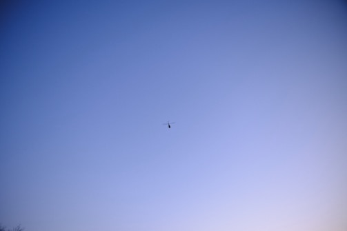 A helicopter flying over an open airfield during clear weather.