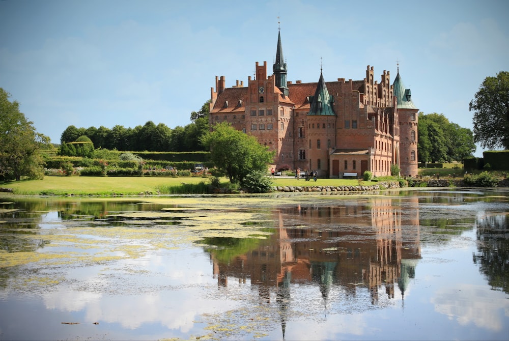 brown castle near green grass field and body of water during daytime