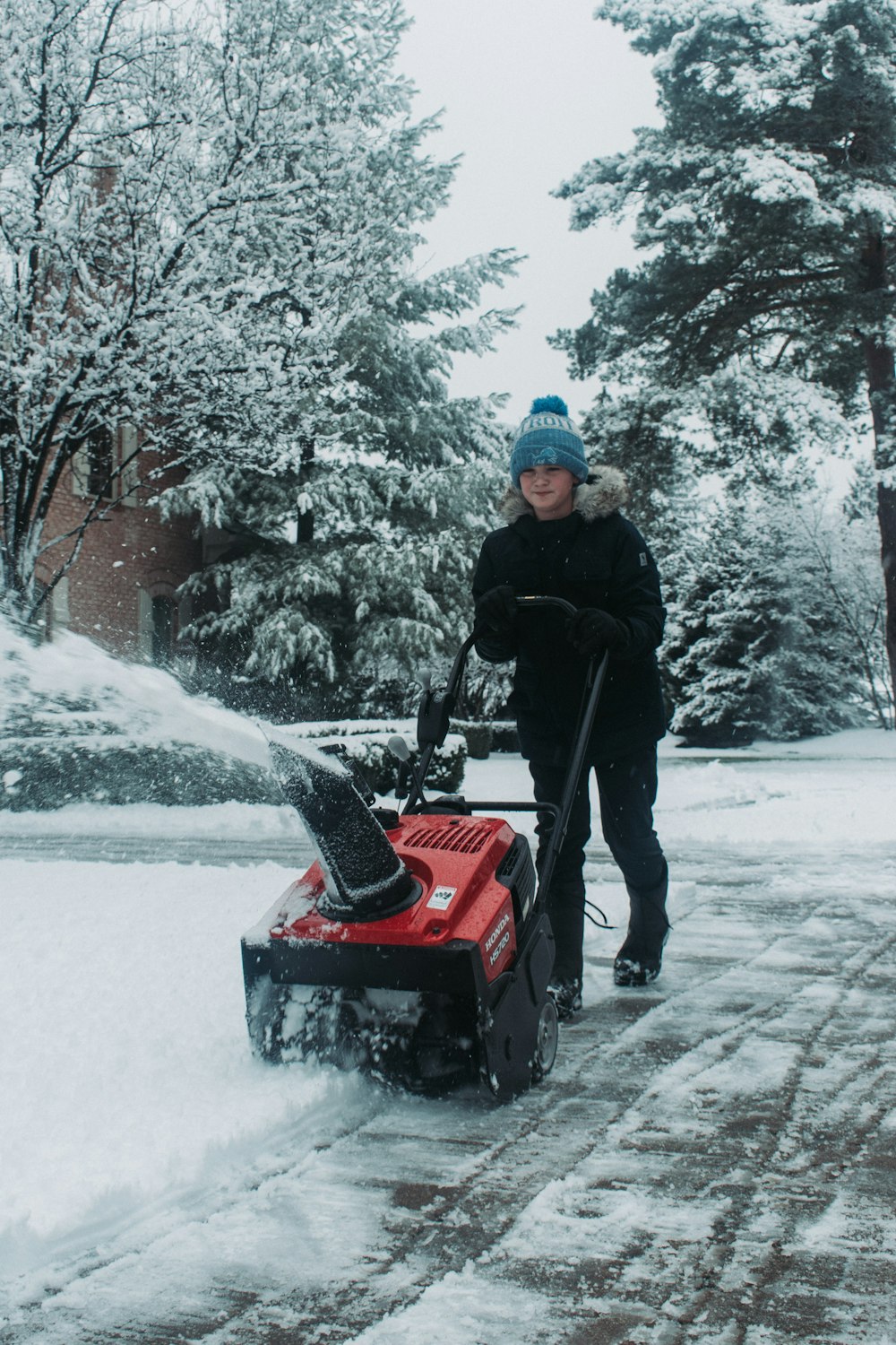 man in black jacket riding red snow blower