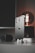 A sleek smartphone with a metallic finish stands upright on a table alongside a modern smartwatch, wireless earbuds, and a glowing antique-style bulb. The scene is set against a dark background, emphasizing the shiny surfaces and elegant technology.
