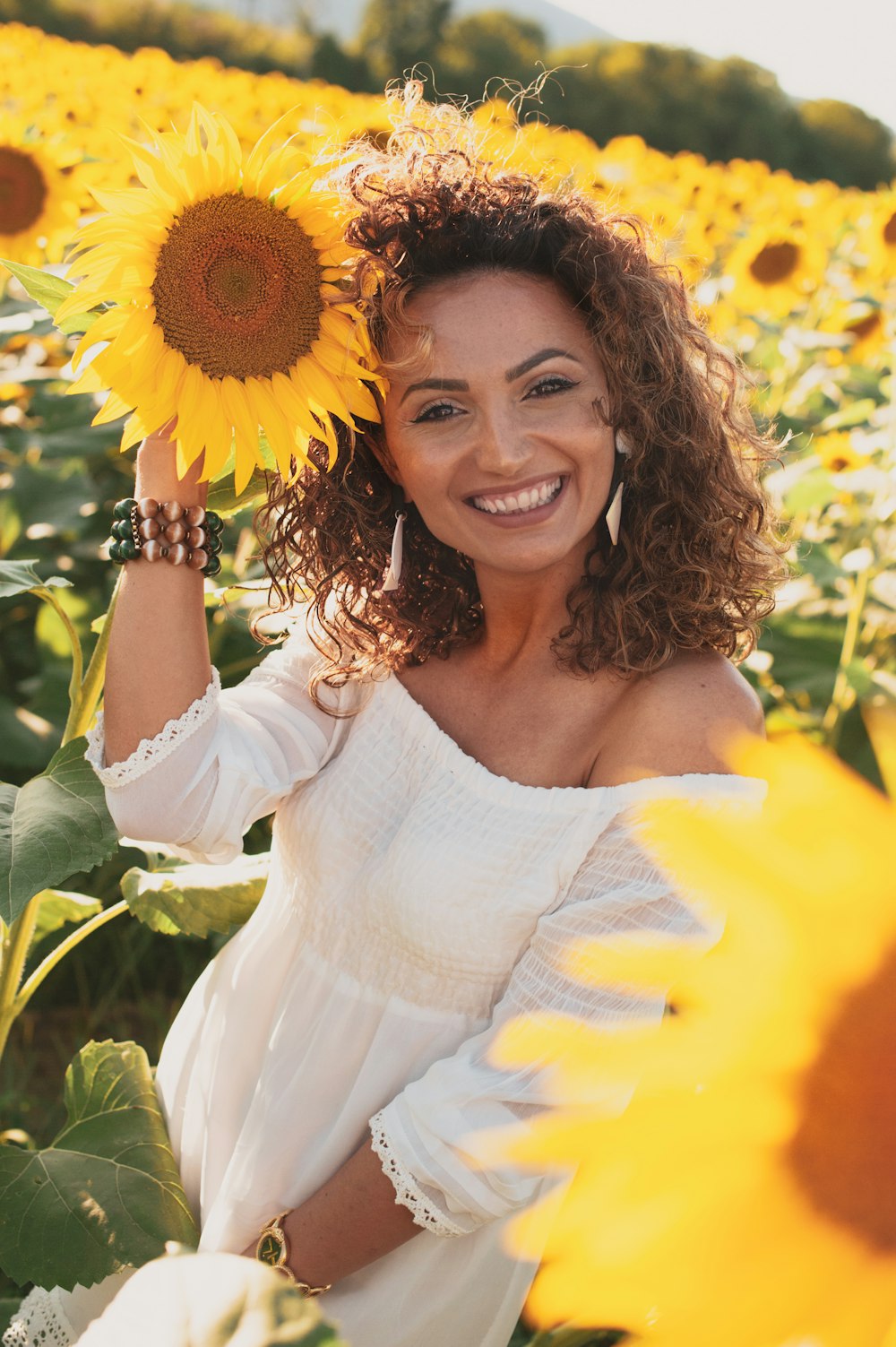 smiling woman in white off shoulder dress holding sunflower