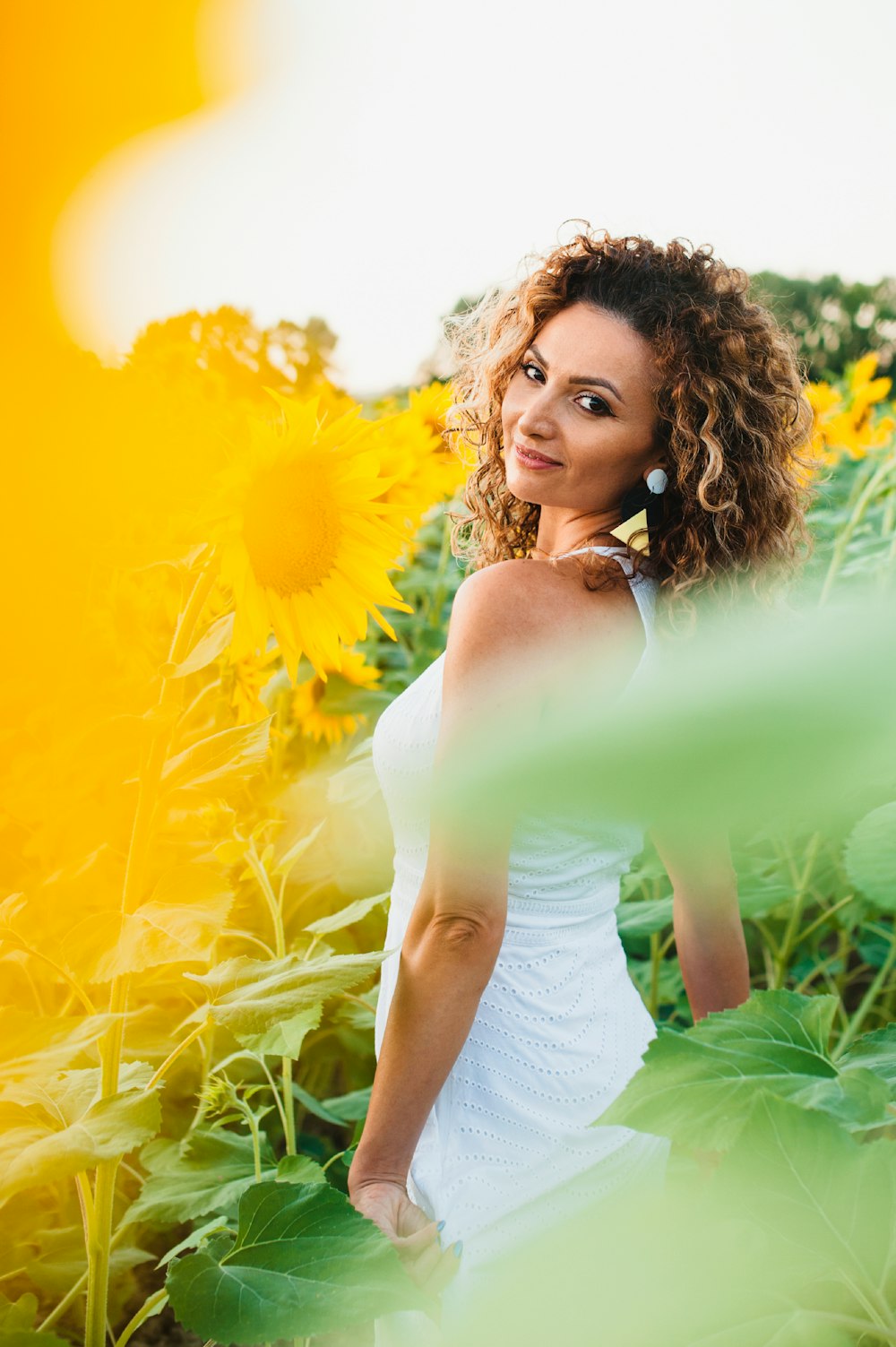 woman in white tank top standing on sunflower field during daytime