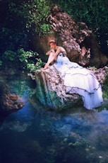 woman in white dress sitting on rock in water