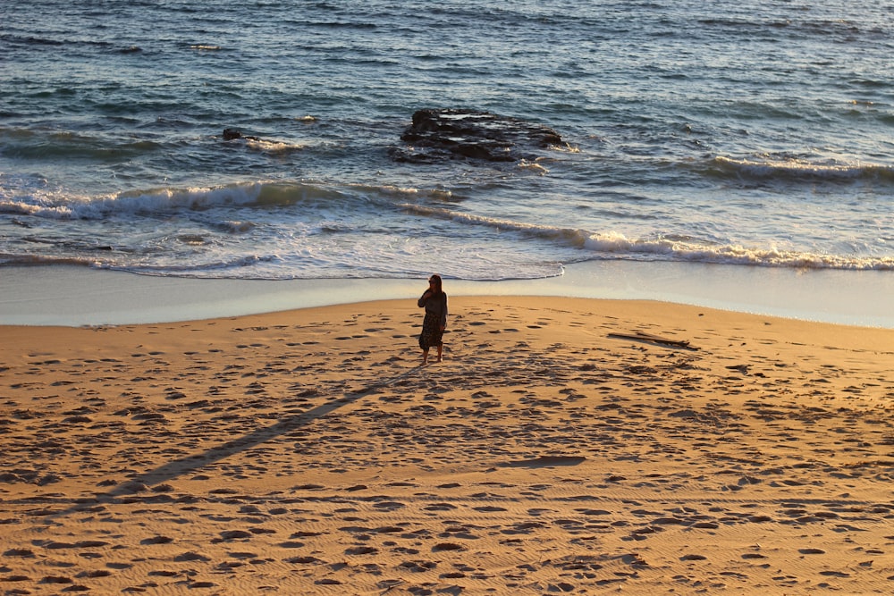 woman in black dress walking on beach during daytime