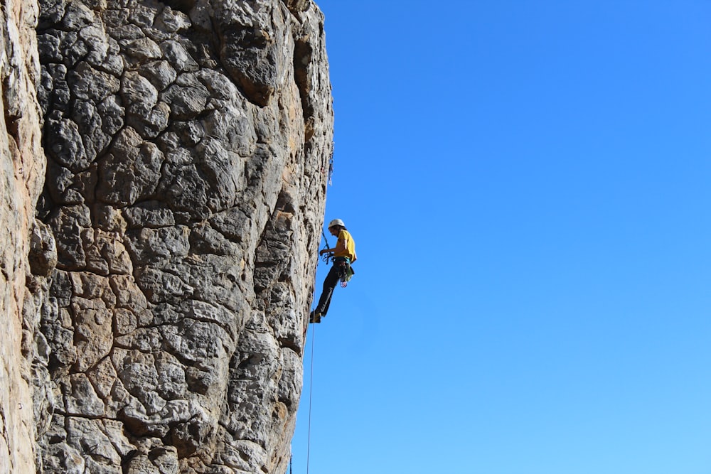 man in yellow jacket climbing on rocky mountain during daytime