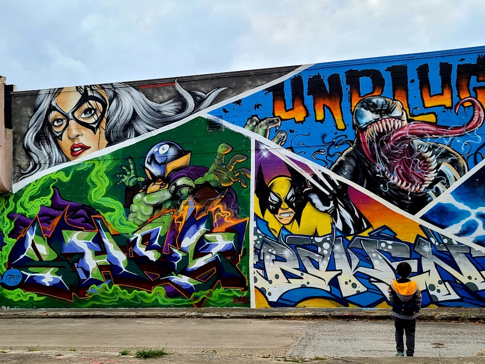 man in black jacket and black pants standing beside graffiti wall during daytime