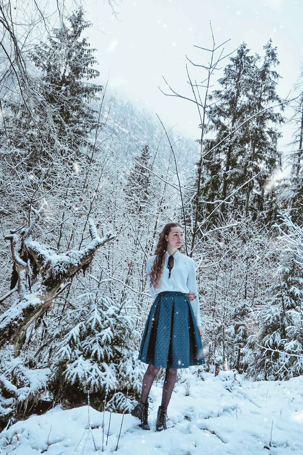 woman in white long sleeve shirt and blue skirt standing on snow covered ground