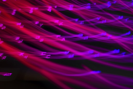 Bright neon colors creating a dynamic effect with blurred lines. Letters are scattered across the image in a distorted and artistic manner.