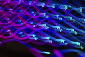 A dynamic, abstract display of neon-colored letters, possibly from a keyboard, with a motion blur effect. The image is dominated by swirling patterns of purple, blue, and cyan hues that create a sense of movement.