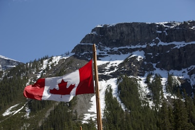 A welcoming Canadian maple leaf flag waving in front of a snowy mountain backdrop.