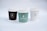 Three coffee cups with lids are arranged side by side. Each cup has a logo and the name 'Guernica Coffee & Patisserie' printed on it. The cup on the left is dark brown, the middle one is green, and the one on the right is white. The background is a soft white, creating a minimalist and clean aesthetic.