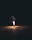 A single firework sits on the ground emitting bright sparks and trails of light against a dark backdrop. The surrounding area is dimly illuminated by its glow, highlighting the stark contrast between the intense brightness of the firework and the surrounding darkness.
