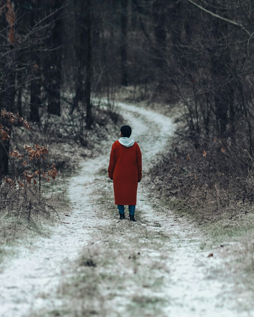 person in red coat walking on pathway between trees during daytime